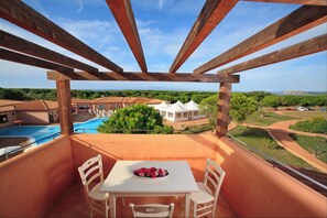 A balcony with a table and chairs, overlooking a swimming pool and a villa. - Cozy Studio With Shared Pool (Aglientu)