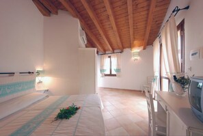 A bedroom with a wooden ceiling, a bed with a floral arrangement, a bedside table, and a television. - Cozy Studio With Shared Pool (Aglientu)
