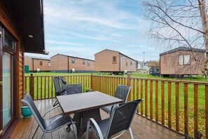 Een terras met een tafel en stoelen, een houten hek en een uitzicht op verschillende gelijksoortige gebouwen op de achtergrond.
