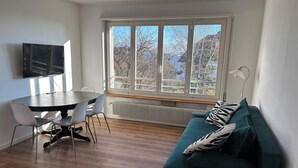 Ein modernes Wohnzimmer mit Essbereich, großen Fenstern, einem Flachbildfernseher und einem grünen Sofa.