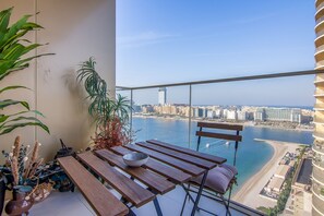 Un balcon avec une table en bois, une chaise et une vue sur le paysage urbain et l’eau.