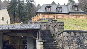 A stone staircase leading to a wooden deck with a stone wall and a building with a stone facade and a sloped roof. - Maison Auvergnate Le repaire des Milans (Laveissière)