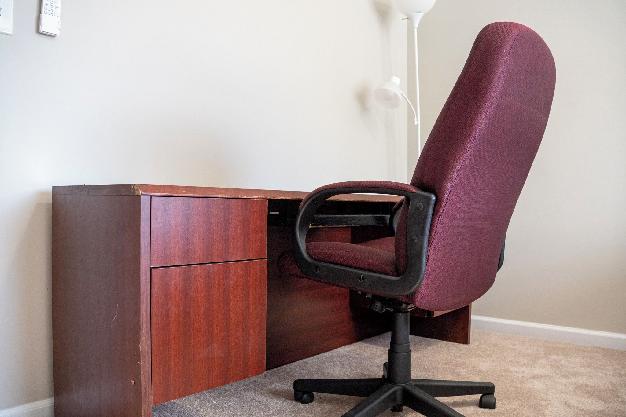 A wooden desk with a red office chair and a white lamp.