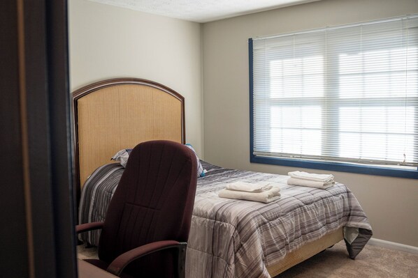 A bedroom with a bed, a chair, and a window with blinds. - Charming 3 Bedrooms with Spacious Living and Convenient Location to Shopping & Interstate (Lawrenceville)