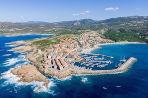 An aerial view of a coastal town with a marina, rocky coastline, and surrounding hills. - Functional Studio With Shared Pool (Aglientu)