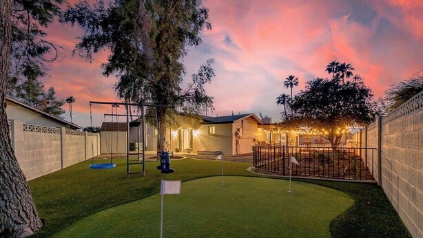A backyard with artificial grass, a swing set, and a fenced area. - Desert Oasis in Mesa- Poolside & Hot Tub (Mesa)