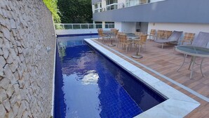A swimming pool with a tiled edge, surrounded by wicker chairs and a table on a wooden deck. - COOND0105 - Ondina Residence (Salvador)