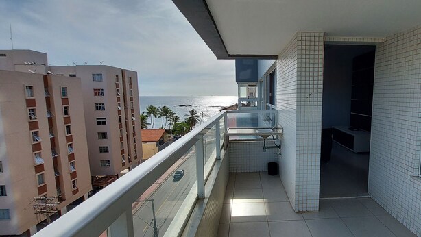 A balcony with a view of the ocean, a tiled wall, and a door leading to a room. - COOND0105 - Ondina Residence (Salvador)