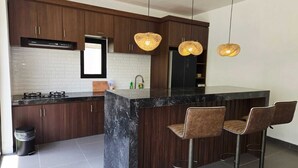 Une cuisine moderne avec des meubles en bois foncé, un îlot central en marbre noir et trois suspensions lumineuses en fibres tressées.