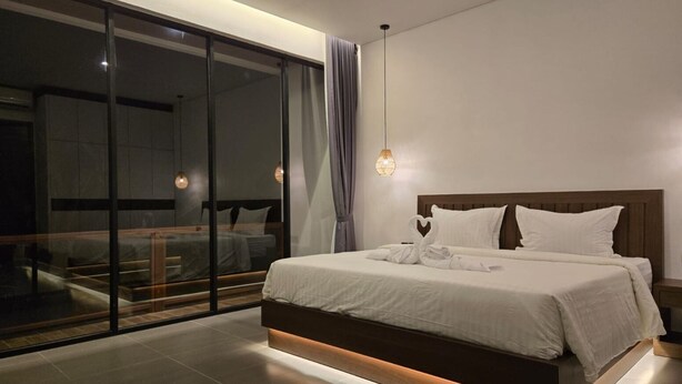 Une chambre moderne avec un grand lit, une porte vitrée donnant sur un balcon et un luminaire suspendu.