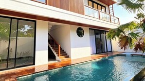 Une maison moderne à deux étages, dotée d’une piscine, de grandes fenêtres et d’une terrasse en bois.