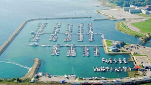 Vista aérea de un puerto deportivo con numerosas muelles y barcos, rodeado de un paisaje natural y un conjunto de edificios.