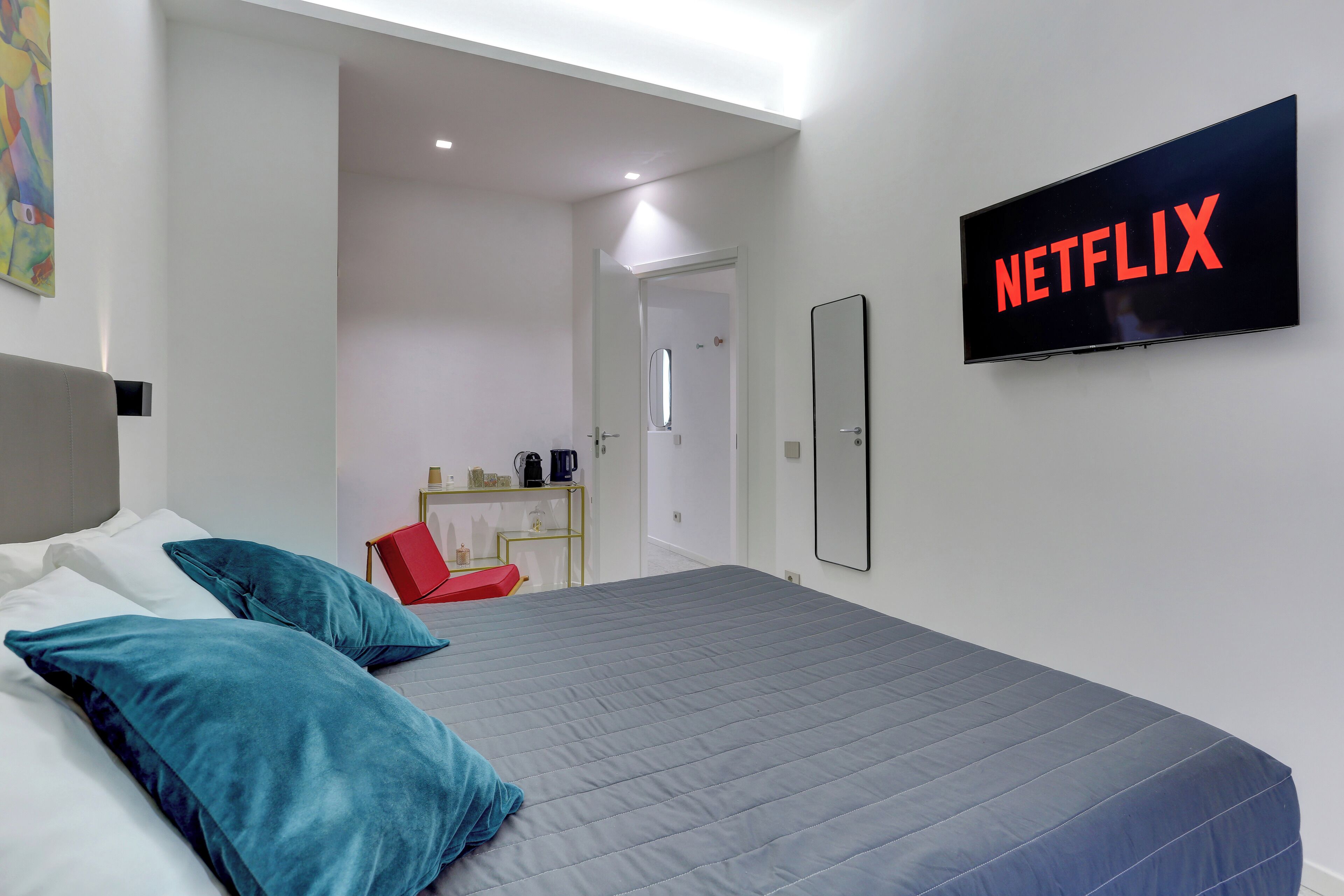 A modern hotel room with a large bed, a flat-screen TV mounted on the wall, and a small desk with a chair.