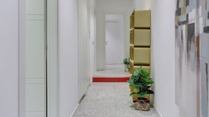 Un couloir avec un tapis rouge menant à une porte, une plante en pot et une bibliothèque de couleur dorée.