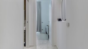 Un couloir étroit, avec une porte blanche au fond, qui donne sur une salle de bain équipée d’une douche et de toilettes.