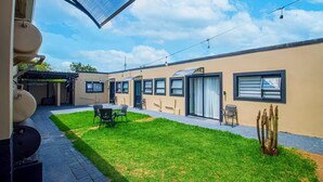 Un patio moderno al aire libre con una mesa de comedor, sillas y una pequeña zona ajardinada.