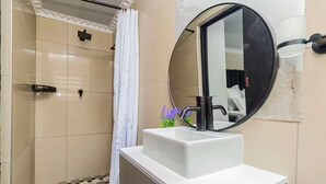 Un baño con un lavamanos blanco, un grifo negro y un espejo redondo.