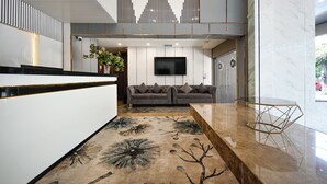 Een moderne lobby met een receptiebalie, een bank, een televisie en een decoratief vloerkleed.