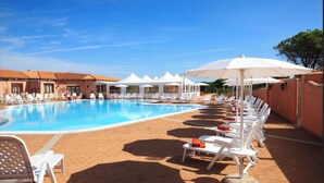 A pool area with lounge chairs and umbrellas, surrounded by buildings with tiled roofs. - Comfy Studio With Pool (Aglientu)