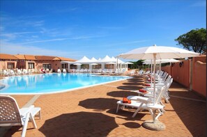 Zona de piscina con sillas de descanso y sombrillas, rodeada de edificios con techos de tejas.