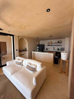 A modern living room with a white sofa and a kitchen area in the background. - Sea Breeze Penthouse at Conchas Chinas (Puerto Vallarta)