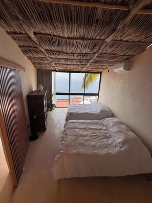 A room with a thatched ceiling, two beds, a wardrobe, and a view of the sea. - Sea Breeze Penthouse at Conchas Chinas (Puerto Vallarta)