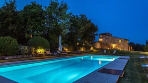 A rectangular swimming pool with a stone building in the background, surrounded by trees and outdoor seating. - Podere Pisinano- Tuscan villa with swimming pool (Toscana)