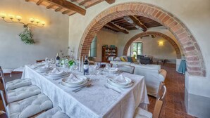 A dining area with a long table set for a meal, brick arches, and a cozy seating area with cushions. - Podere Pisinano- Tuscan villa with swimming pool (Toscana)