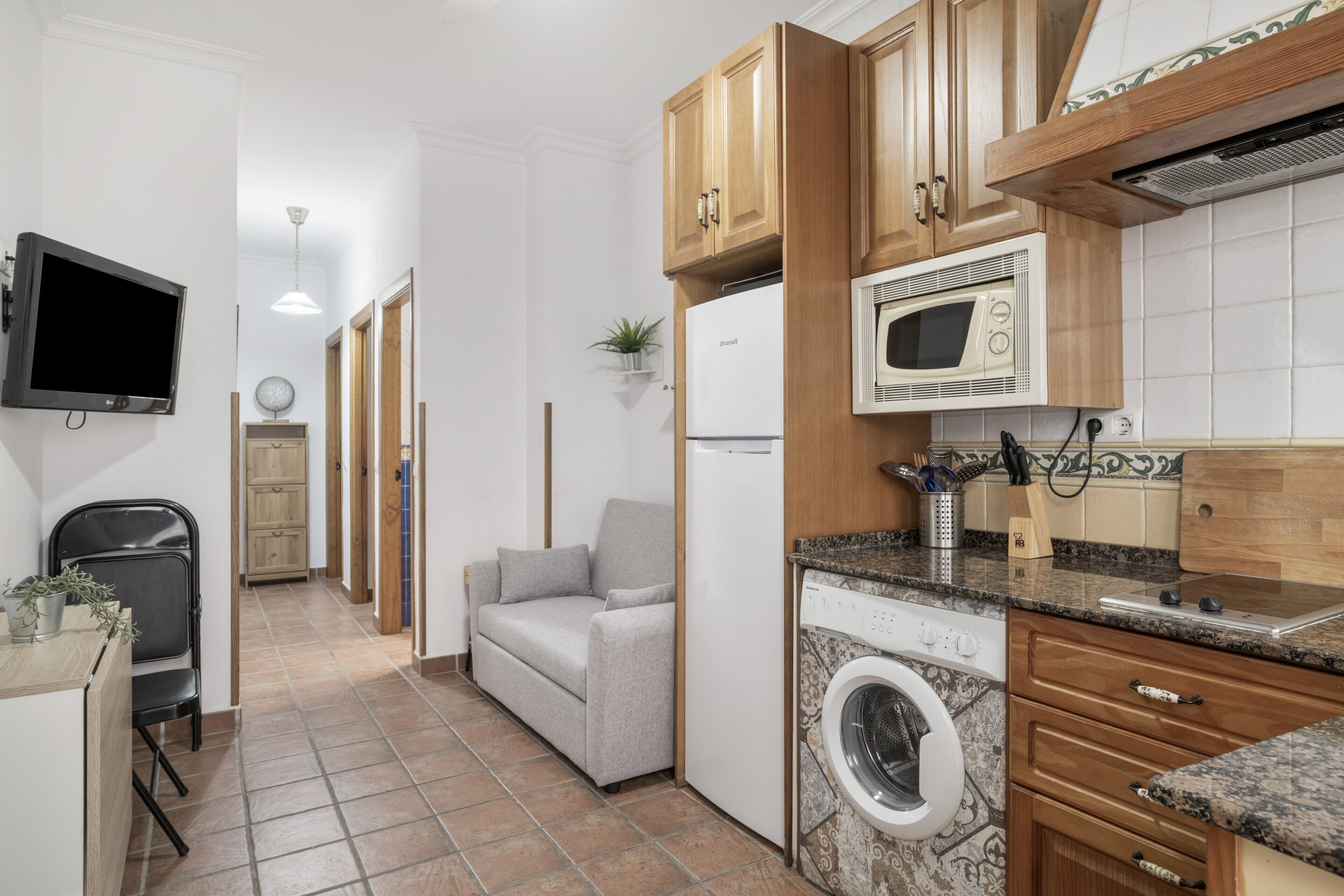 A compact kitchen with a microwave, washing machine, and wooden cabinets.