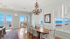 A dining area with a wooden table and white wicker chairs, large windows with ocean views, and a chandelier. - Rooftop Deck, Paddle Boards, Gulf Front on 30A (Inlet Beach)