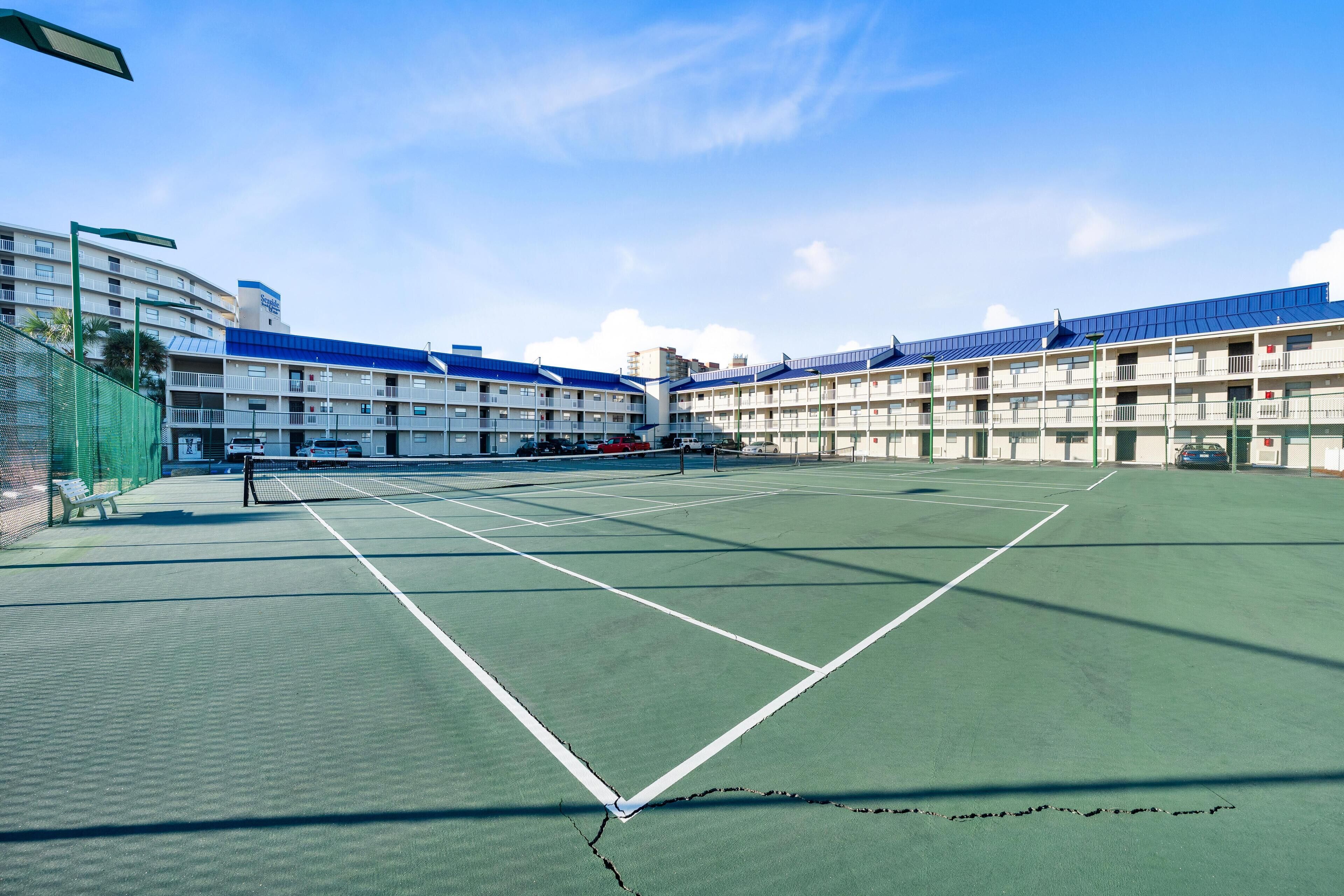 Ein Tennisplatz mit Netz, umgeben von einem Mehrstöckiger Gebäude mit Balkonen.