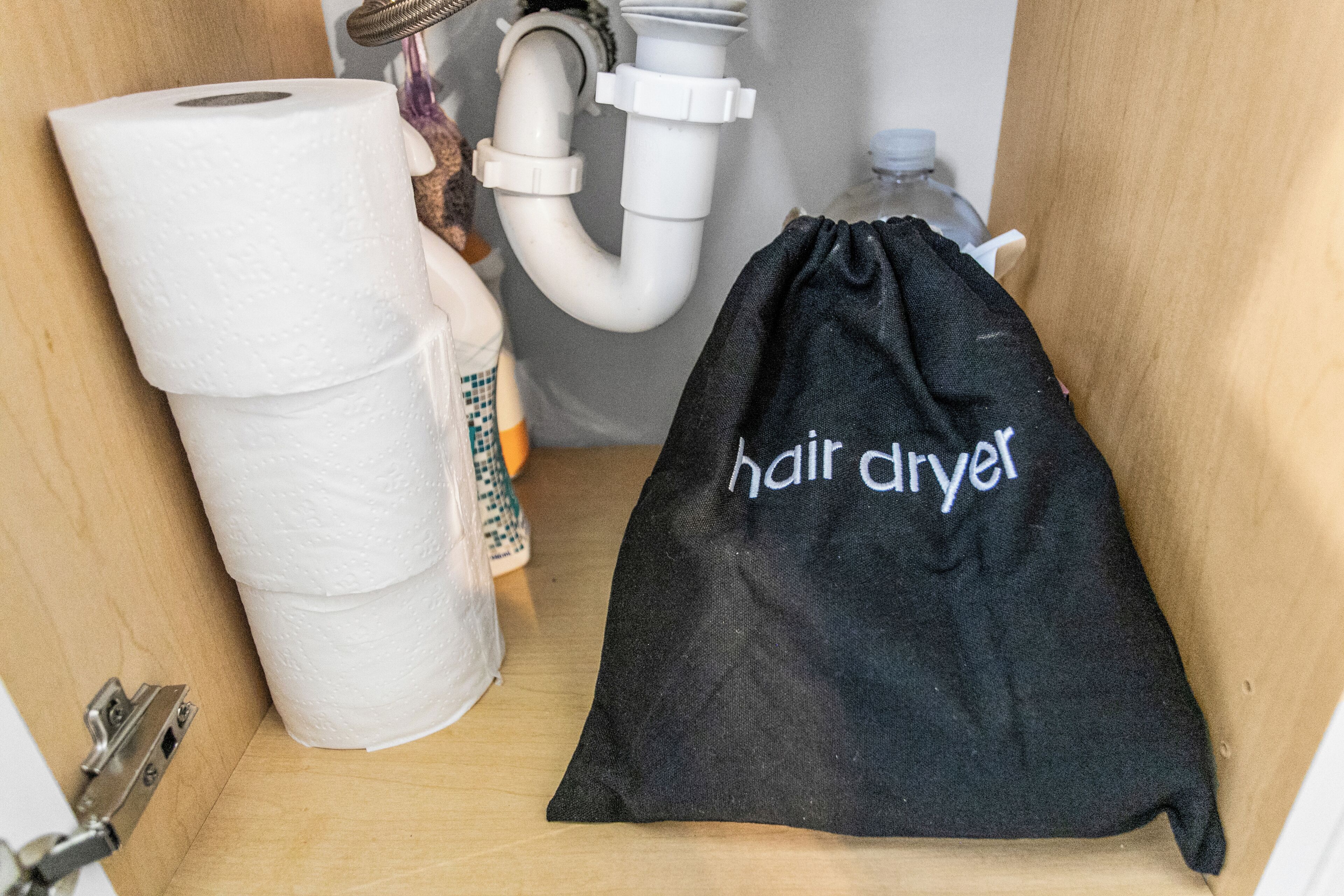 A bathroom with a toilet paper roll, a hair dryer, and a black bag labeled "hair dryer".