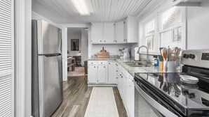 Moderni keittiö, jossa on valkoiset kaapit, ruostumattomasta teräksestä valmistetut kodinkoneet ja puulattia.
