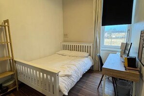 A bedroom with a single bed, a desk with a chair, a radiator, and a window with curtains. - 2 Bed Flat - Sleeps 4 - Parking - Wifi (Glasgow)