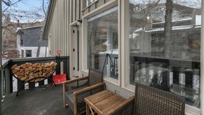 Un espace extérieur aménagé, abrité et doté d’une pile de bois de chauffage, de meubles en osier et de grandes fenêtres offrant une vue sur les environs.