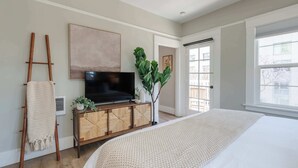 Une chambre moderne avec un grand lit, une télévision, une plante et une échelle appuyée contre le mur.