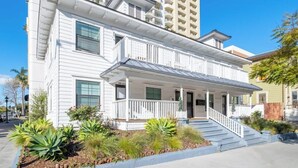A two-story building with a balcony on the second floor, a covered front porch, and a small garden area with plants. - Sunny Stylish & Central - Luxe Little Italy Studio (San Diego)