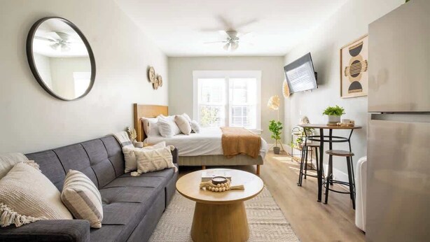 A compact living space with a sofa, a round coffee table, a bed, a TV, and a kitchen area. - Sunny Stylish & Central - Luxe Little Italy Studio (San Diego)
