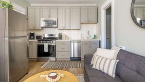 A compact kitchen with modern appliances, a grey sofa, and a round wooden table. - Sunny Stylish & Central - Luxe Little Italy Studio (San Diego)