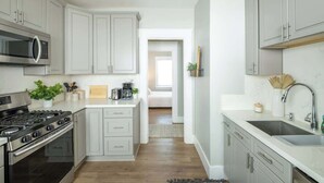 A modern kitchen with grey cabinets, a stainless steel stove, a microwave, and a sink. - Chic Little Italy Apt | Balcony | Walk Everywhere! (San Diego)