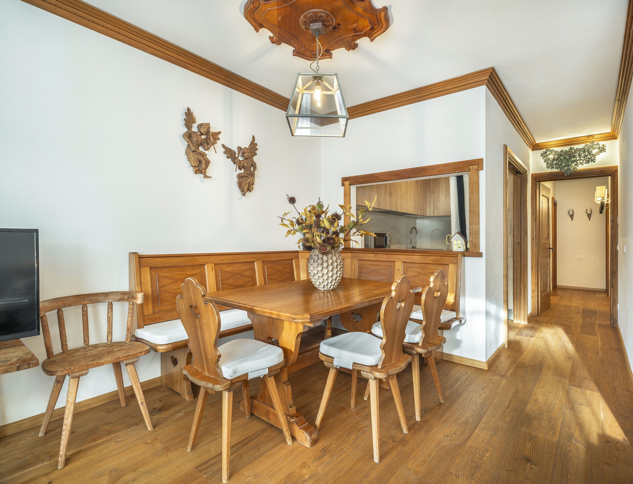 A dining area with a wooden table and chairs, a vase with flowers, and a kitchen in the background.