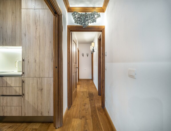 Un couloir avec un plancher en bois, un coin cuisine avec des placards et un luminaire au plafond.