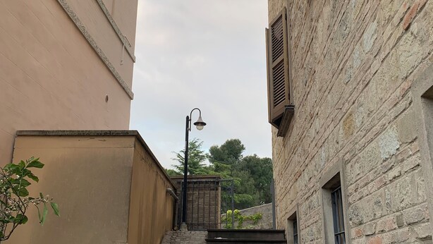 Une ruelle étroite avec un escalier en pierre menant à un immeuble à la façade en pierre et doté d’un portail en métal.