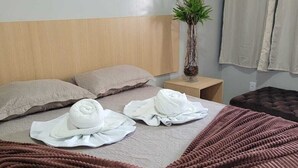 Ein ordentlich bezogenes Bett mit einer braunen, strukturierten Decke, zwei Kissen und zwei aufgerollten Handtüchern.