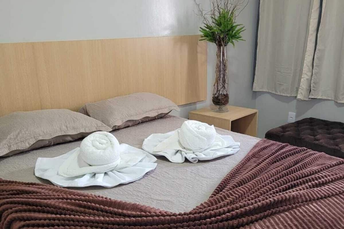 Ein ordentlich bezogenes Bett mit einer braunen, strukturierten Decke, zwei Kissen und zwei aufgerollten Handtüchern.