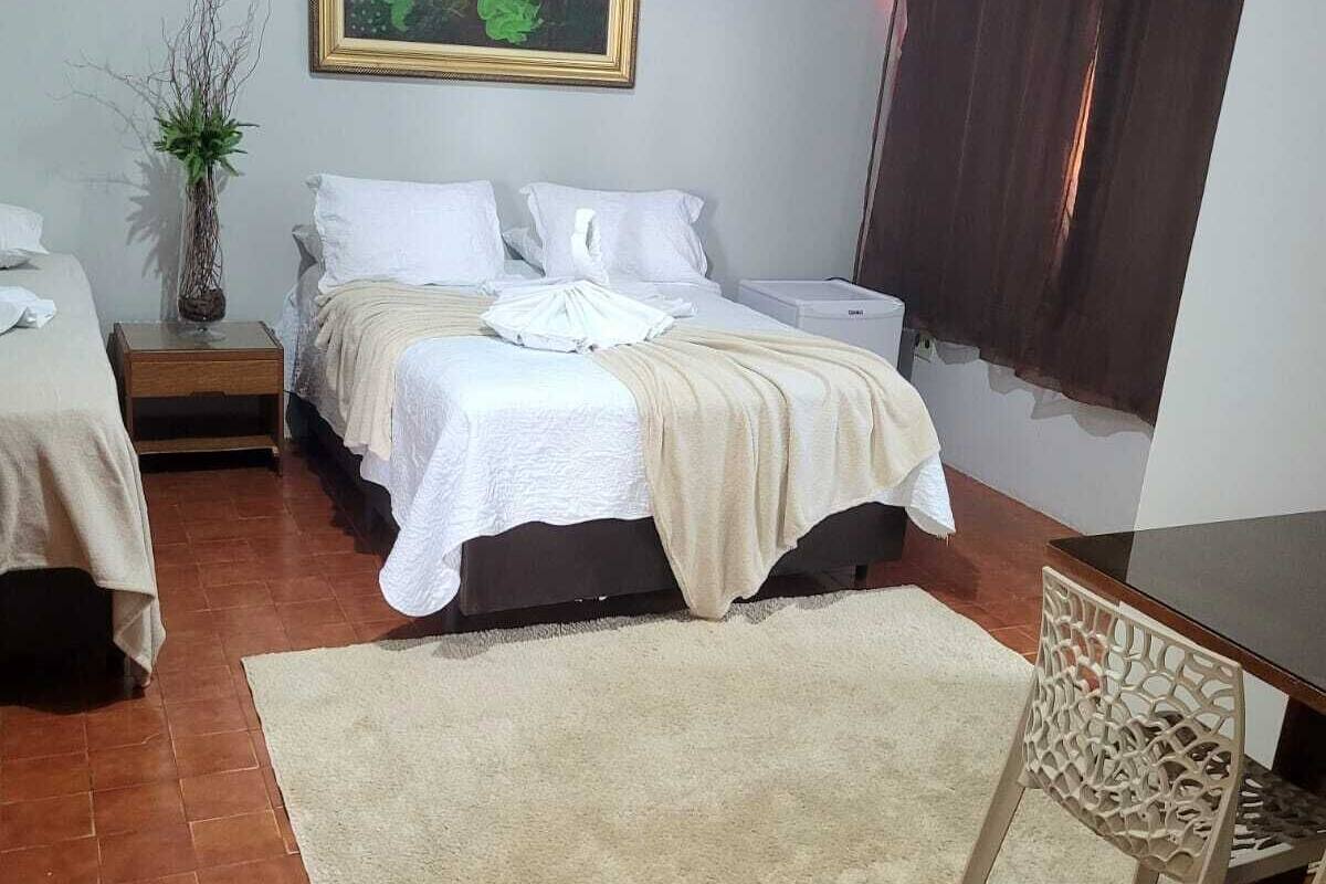 Ein Schlafzimmer mit zwei Betten, einem Schreibtisch, einem Stuhl, einer Topfpflanze und einem Bild an der Wand.