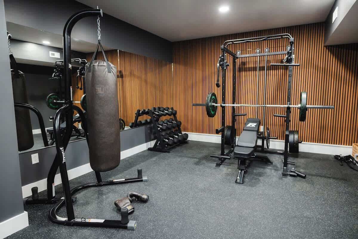A home gym with a punching bag, weight bench, dumbbells, and a squat rack.