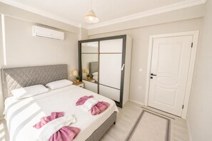 Ein Schlafzimmer mit Bett, Nachttischen, einem Spiegel, einem Kleiderschrank und einer Klimaanlage.