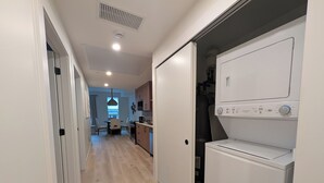 Una cocina moderna con lavadora y secadora integradas, un comedor con mesa y sillas, y un pasillo que conduce a una sala de estar.