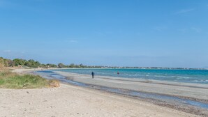 Ein Strand mit blauem Himmel, sandigem Ufer und einer Person, die spazieren geht.